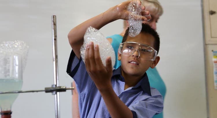 Student wearing safety glasses and doing a science experiment with frothy bubbles in his hands