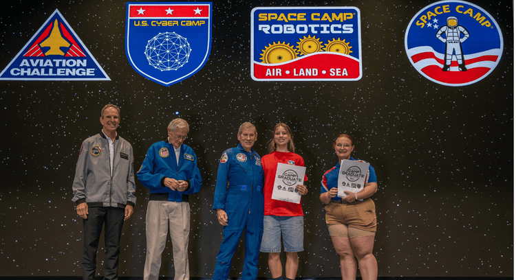 Student graduating from a USA Space camp receiving graduation certificate from astronaut-looking people