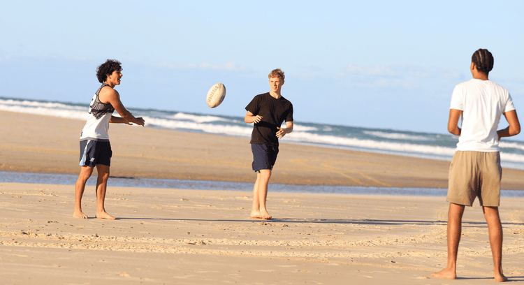 Three boys in casual clothes throwing a football around on the beach
