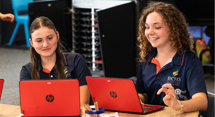 Two female students working on laptops with a smile