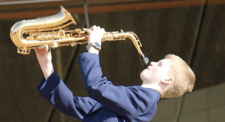 Male student playing saxophone while lifting it high in the air