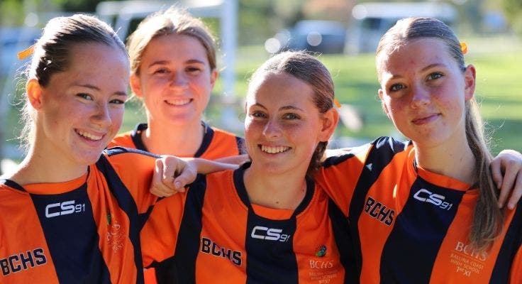 Close up of four female soccer players smiling with arms around each other