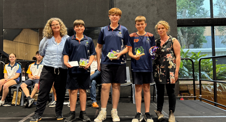 3 young male students holding STEM trophies with female teacher either side