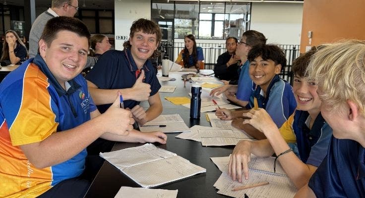 Group of boys in class doing work, smiling and giving thumbs up