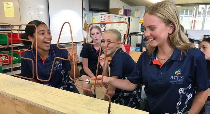 Laughing girls trying to navigate a hand-held hoop up and over metal shapes without touching the sides